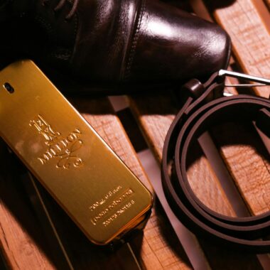 Elegant black luxury glossy man shoes and belt composing with perfume in bottle in form of gold bar on wooden bench