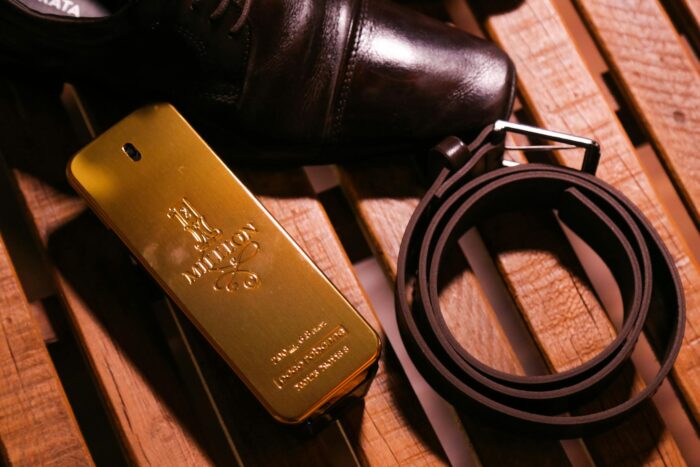 Elegant black luxury glossy man shoes and belt composing with perfume in bottle in form of gold bar on wooden bench